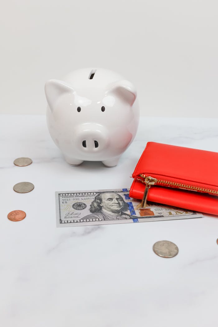 White piggy bank with coins and a red wallet on a marble desk.